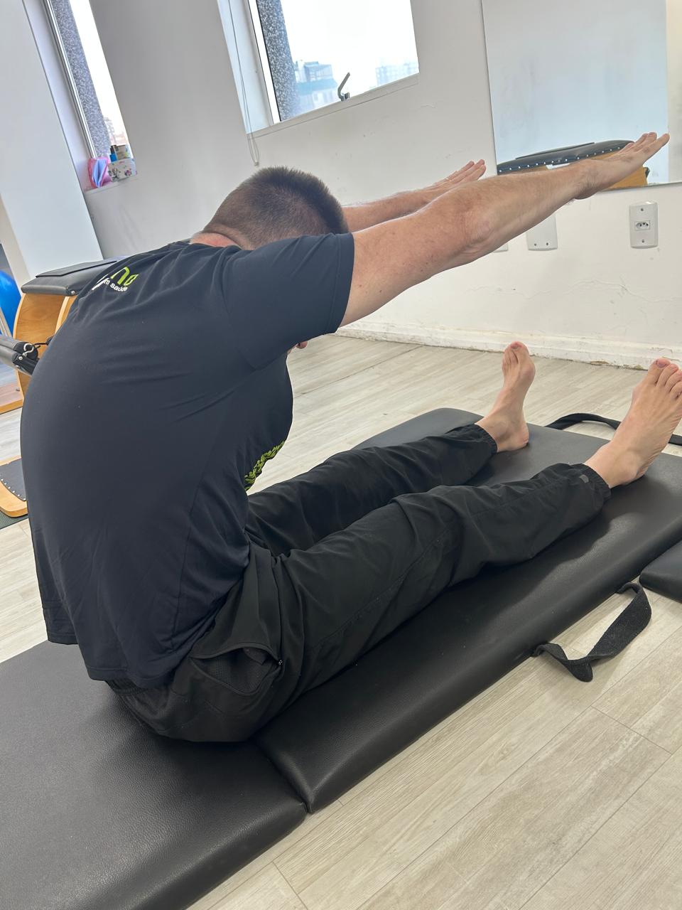 Aluno em exercício de flexão de coluna no solo durante sessão de Pilates.