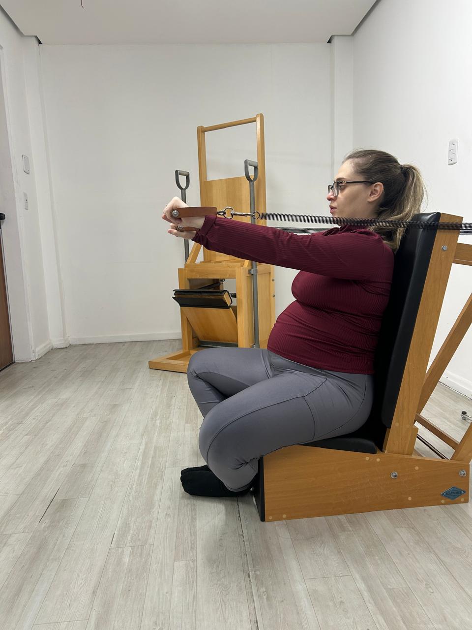 Gestante realizando movimento de alcance no equipamento de Pilates durante atendimento individual.