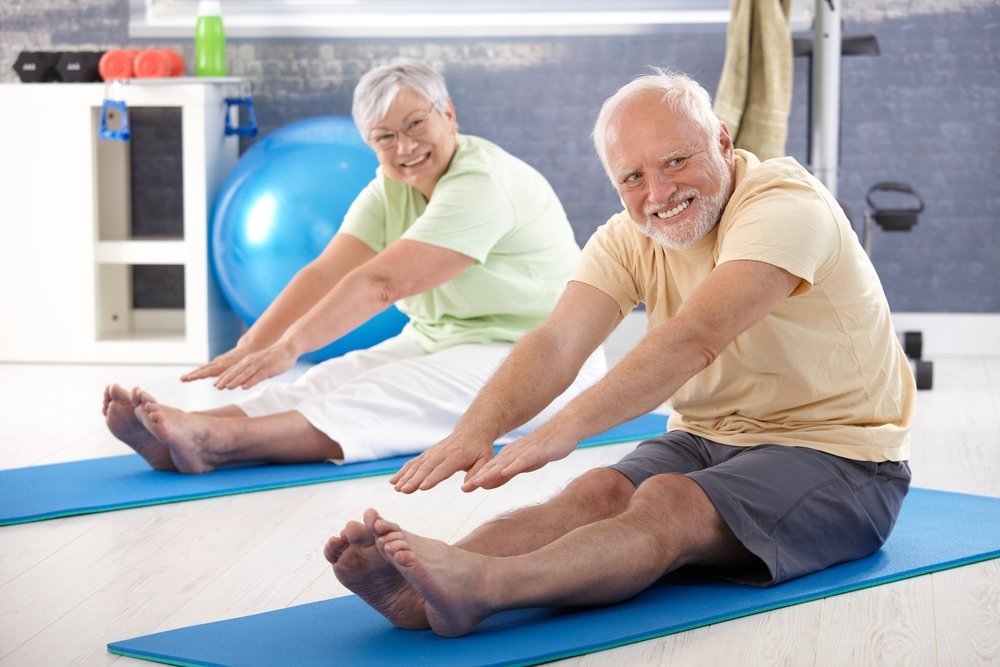 Idosos em exercício de alongamento no solo.